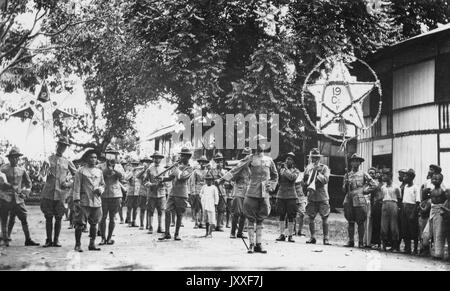 Afroamerikanische Soldaten marschieren zusammen mit einigen nicht-Armeemitgliedern in einer Parade, die meisten Armeemänner spielen Instrumente, es gibt zwei größere Sternzeichen, ein Stern hat die Nummer 19 darauf, es gibt afroamerikanische Jungen, die schauen, 1920. Stockfoto