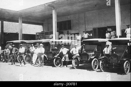 Afroamerikanische Männer warten neben ihren geparkten Autos für Passagiere, die Autos sind möglicherweise in einer Garage aufgereiht, 1920. Stockfoto