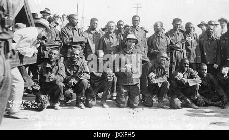 Vollständige Landschaftsaufnahme amerikanischer Soldaten, die meisten afroamerikanischen, Uniformen, zwei Reihen Männer, erste Reihe knieend mit einigen Männern, die kleine Blumensträuße halten, neutrale/glückliche Gesichtsausdrücke, 1917. Stockfoto