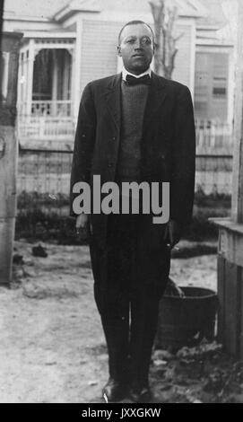 Ganzkörperportrait eines afroamerikanischen Mannes, der Anzug, Füße zusammen, Hände an Seite, im Freien, neutraler Gesichtsausdruck, 1910. Stockfoto