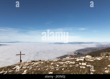 Ein hölzernes Kreuz auf der Spitze des Monte Subasio Berg, mit einem Meer von Nebel unten Stadt Assisi (Umbrien) im Hintergrund und Stockfoto