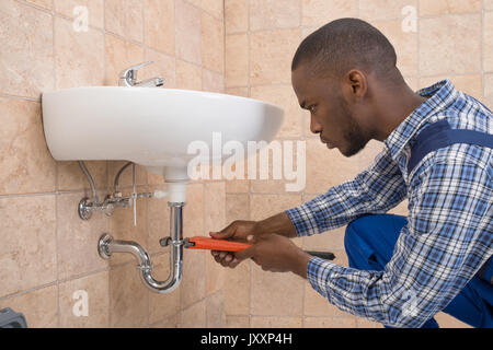 Junge afrikanische Mann Klempner Instandsetzung Waschbecken im Badezimmer Stockfoto