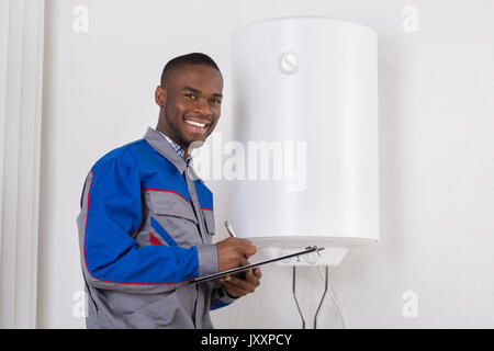 Junge afrikanische Mann Klempner Holding Zwischenablage auf Elektroboiler Stockfoto