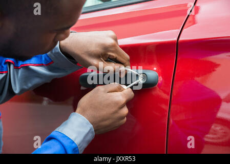 Junge männliche Mechaniker Holding Lockpicker zu Öffnen rotes Auto Tür Stockfoto