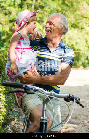 Opa lachend auf dem Fahrrad mit seiner Enkelin Stockfoto