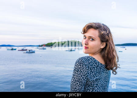 Junge glücklich lächelnde Frau sitzt auf der Kante des Dock in Bar Harbor, Maine, über der Schulter Stockfoto