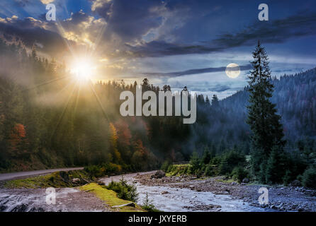 Tag und Nacht Zeit ändern Konzept über nebligen Wald und Fluss. Wunderschöne herbstliche Landschaft in den Bergen mit Sonne und Vollmond Stockfoto