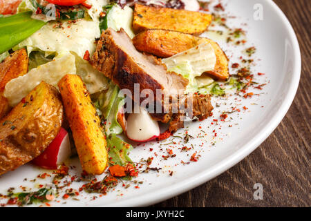 Das Essen im Restaurant, leckeres Essen, gebratene Nahrungsmittel-Salat mit frischem Gemüse Gegrilltes Kalbfleisch und gebackene Kartoffeln auf dem Teller auf einen hölzernen Tisch. Stockfoto