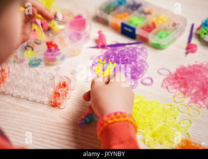 Außerschulische Aktivitäten, Gruppe, Bildung und Handarbeit Konzept - Hände das Weben von farbigen rubber band Bracelet, Nahaufnahme, Holz- Hintergrund Stockfoto