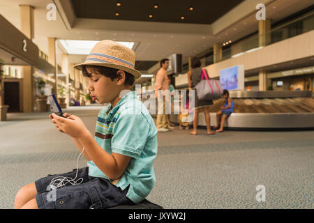 Junge spielt auf Handy im Flughafen Stockfoto