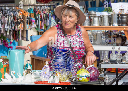 Frau Inhaber Verkauf bric-a-brac auf Herne Bay, Kent. Andere Stände enthalten tankards, Glaswaren und Kleidung. Stockfoto
