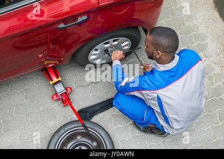 Junge afrikanische Mechaniker ändern Reifen eines Autos mit einem Schraubenschlüssel Stockfoto