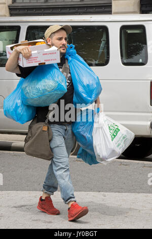 Einer überlasteten Mann sechs Einkaufstaschen tragen, Schultergurt und eine Kiste Verlassen des Union Square grünen Markt in New York City. Stockfoto