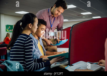 Schüler arbeiten an Computern mit Lehrbüchern. Eine männliche Lehrer ist, bei ihnen stehen und ihnen helfen, mit ihrer Arbeit. Stockfoto