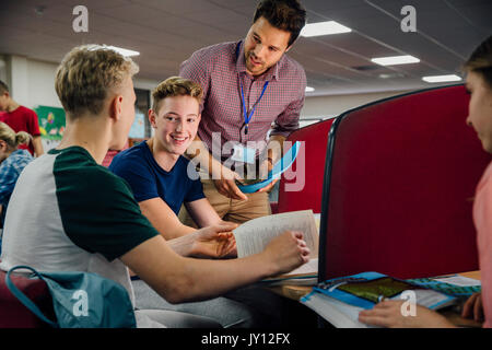 Schüler arbeiten an Computern mit Lehrbüchern. Eine männliche Lehrer ist, bei ihnen stehen und ihnen helfen, mit ihrer Arbeit. Stockfoto