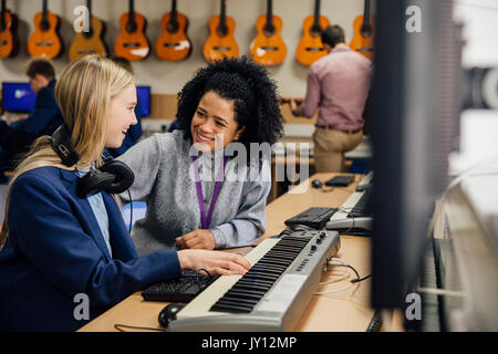 Lehrerin sitzt mit einem ihrer Schüler im Musikunterricht in der Schule. Sie lernt, um auf der Tastatur zu spielen und ist das Tragen von Kopfhörern. Stockfoto
