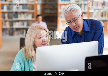 Ältere Menschen helfen Frau mit Computer in der Bibliothek Stockfoto