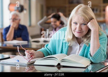 Ältere Frau mit Buch in der Bibliothek verwirrt Stockfoto