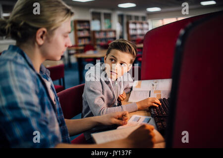 Junge Student arbeitet mit einem älteren Schüler arbeiten zu fangen. Sie reden und diskutieren, was im Lehrbuch und der kleine Junge ist Stockfoto