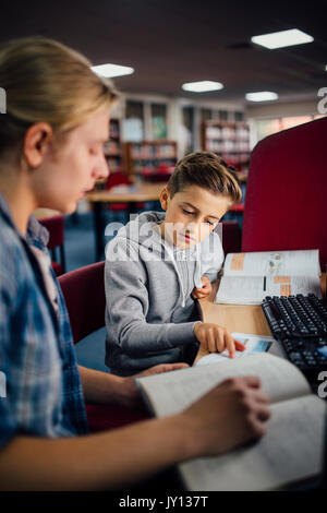 Junge Student arbeitet mit einem älteren Schüler arbeiten zu fangen. Sie reden und etwas diskutieren im Lehrbuch. Stockfoto