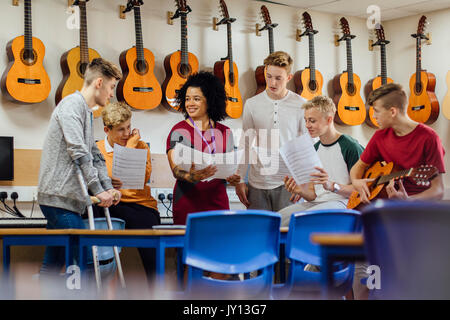 Männliche Jugendliche sind in einem Musikunterricht in der Schule. Sie diskutieren mit Ihrem Lehrer. Stockfoto