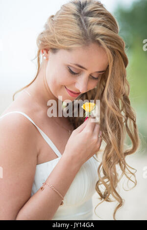 Porträt der jungen Braut im weißen Kleid mit gelbe Blume in der Nähe der Küste im Sommer Abend Stockfoto