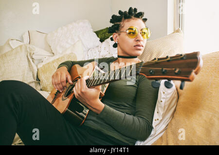 Gemischte Rasse Frau sitzt auf dem Bett, Gitarre zu spielen Stockfoto