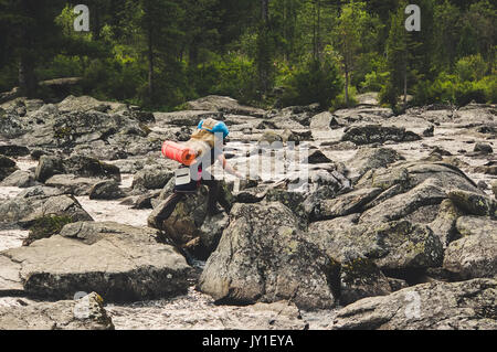 Wanderer ascenting in einem Berge. Touristen mit einem großen Rucksack am Abend durch den Stein schleichen Ablagerungen auf der Bergseite. Stockfoto