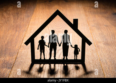 Silhouette von Haus mit Familie Ausschnitt auf hölzernen Schreibtisch Stockfoto