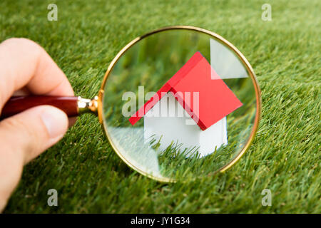 Person Hand mit Lupe Untersuchen ein Modell Haus auf der Wiese Stockfoto