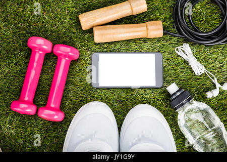 Smartphone mit leerer Bildschirm platziert sind in der Nähe von Trainingsgeräten auf Wiese Stockfoto