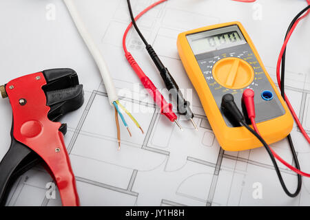 Hohe Betrachtungswinkel des digitalen Multimeters auf Blueprint mit schwarzem und rotem Kabel Stockfoto