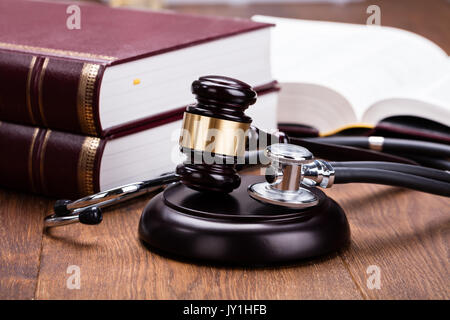 Braun Hammer mit medizinischen Stethoskop in der Nähe von Buch am Schreibtisch aus Holz im Gerichtssaal Stockfoto