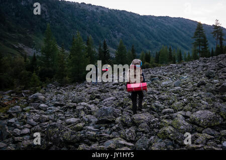 Wanderer ascenting in einem Berge. Touristen mit einem großen Rucksack am Abend durch den Stein schleichen Ablagerungen auf der Bergseite. Stockfoto