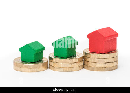 Wohnungsmarkt. British Pound Münzen auf weißem Hintergrund mit roten und grünen Holz Spielzeug Häuser isoliert. Symbole der Anleihen, Kredite, Schulden und Hypotheken Stockfoto