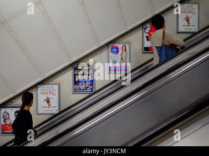 Passagiere lesen die Werbetafeln an der Wand der Rolltreppe an einer Londoner U-Bahn-Station Stockfoto