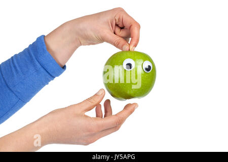 Weibliche Hände halten green apple mit kulleraugen auf weißem Hintergrund mit Kopie Raum isoliert. Gesundes Essen und Lifestyle Konzept Stockfoto