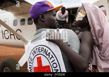 Bor, South Sudan. 18. Juli 2017. Ein Mitglied des Internationalen Komitees vom Roten Kreuz trägt 9-jährige Remaik zu einer Ebene ihr nach Juba, in Bor, Südsudan, 18. Juli 2017 zu evakuieren. Sie war im Kopf ein paar Tage zuvor erschossen, als eine bewaffnete Gruppe junger Männer in ihrem Dorf Vieh zu stehlen. Remaik's Gesicht ist geschwollen und sie kann kaum die Augen öffnen. Foto: Stefanie Glinski/dpa/Alamy leben Nachrichten Stockfoto