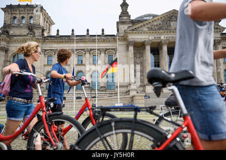 Berlin, Deutschland. 18 Aug, 2017. Die deutsche und die EU-Fahnen auf Halbmast vor dem Reichstag fliegen während Touristen ihre Fahrräder in Berlin, Deutschland, 18. August 2017. Flaggen auf Halbmast in allen öffentlichen Gebäuden in der deutschen Hauptstadt in conmemoration der Terroranschlaege in Barcelona geflogen. Foto: Gregor Fischer/dpa/Alamy leben Nachrichten Stockfoto