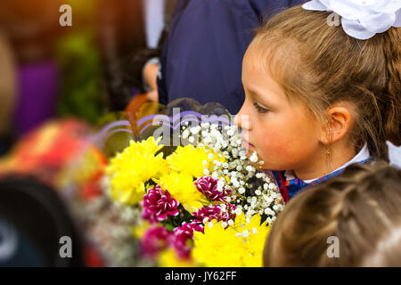 Wenig Erstlingssortierer, Mädchen-Schüler geht auf Wissen Tag zur Schule - September zuerst. Schüler der Grundschule in Uniform mit Bögen und Blumen. Ru Stockfoto