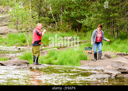 Byglandsfjord, Norwegen - 1 August 2017: Reisedokumentation der Mann seinen Fischen Kleidung vorbereiten, während Frau tragen fangfrischen Fisch in der Hand gefangen. Wald i Stockfoto