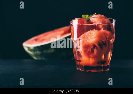 Cocktail mit in Scheiben geschnittenen Wassermelone in einem roten Glas auf einem schwarzen Hintergrund close-up Stockfoto