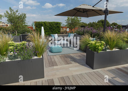 Luxuriöse Dachterrasse in London mit Schnittholz Terassendielen, zeitgenössische Pflanzmaschinen mit üppiger Bepflanzung und moderne Gartenmöbel Stockfoto