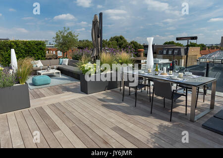 Luxuriöse Dachterrasse in London mit Schnittholz Terassendielen, zeitgenössische Pflanzmaschinen mit üppiger Bepflanzung und moderne Gartenmöbel Stockfoto
