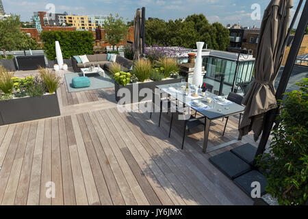 Luxuriöse Dachterrasse in London mit Schnittholz Terassendielen, zeitgenössische Pflanzmaschinen mit üppiger Bepflanzung und moderne Gartenmöbel Stockfoto