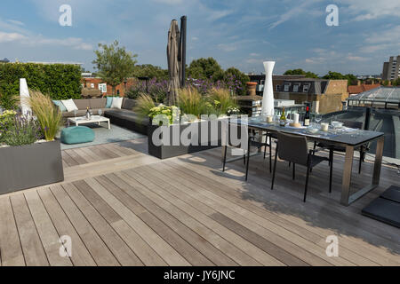 Luxuriöse Dachterrasse in London mit Schnittholz Terassendielen, zeitgenössische Pflanzmaschinen mit üppiger Bepflanzung und moderne Gartenmöbel Stockfoto