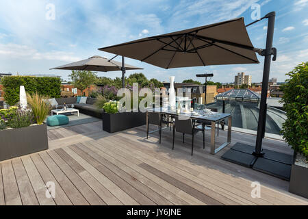 Luxuriöse Dachterrasse in London mit Schnittholz Terassendielen, zeitgenössische Pflanzmaschinen mit üppiger Bepflanzung und moderne Gartenmöbel Stockfoto