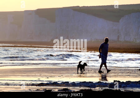 Mann und seinem Hund zu Fuß auf den Strand in der Nähe der berühmten Sieben Schwestern Kreidefelsen, East Sussex. Stockfoto