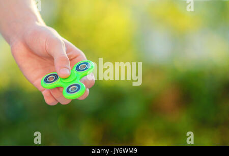 Junge hand mit trendigen zappeln Spinner. Junge spielt mit grünen Spinner im Freien auf der hellen Bokeh. Flache Freiheitsgrad. Stockfoto