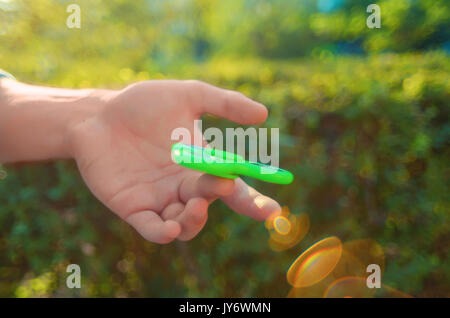 Teenager Hand antistress zappeln Spinner. Junge spielt mit grünen Spinner im Freien bei Sonnenuntergang Strahlen auf die bunten Bokeh. Flache Freiheitsgrad. Stockfoto